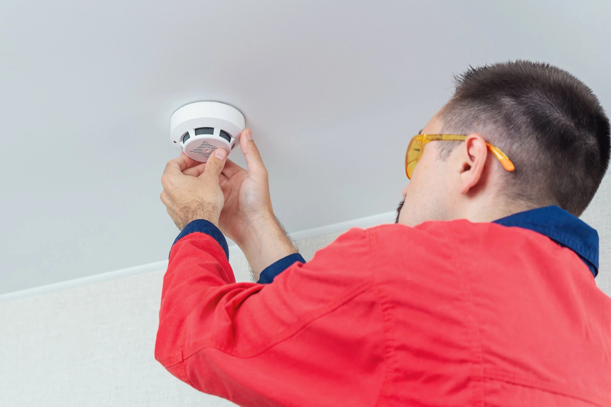 Worker mounting a smoke alarm on a ceiling