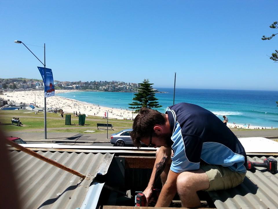 HUX electrician working on a roof for an outdoor lighting install near the beach